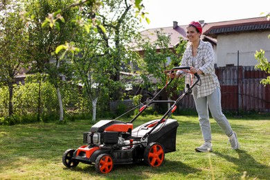 Photo of Smiling woman cutting green grass with lawn mower in garden