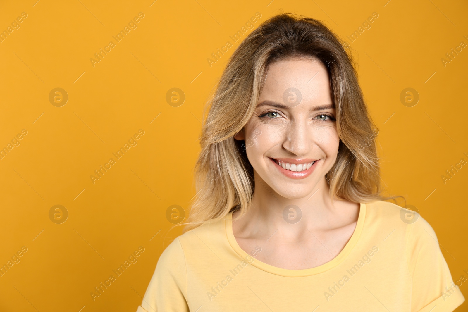 Photo of Portrait of happy young woman with beautiful blonde hair and charming smile on yellow background. Space for text