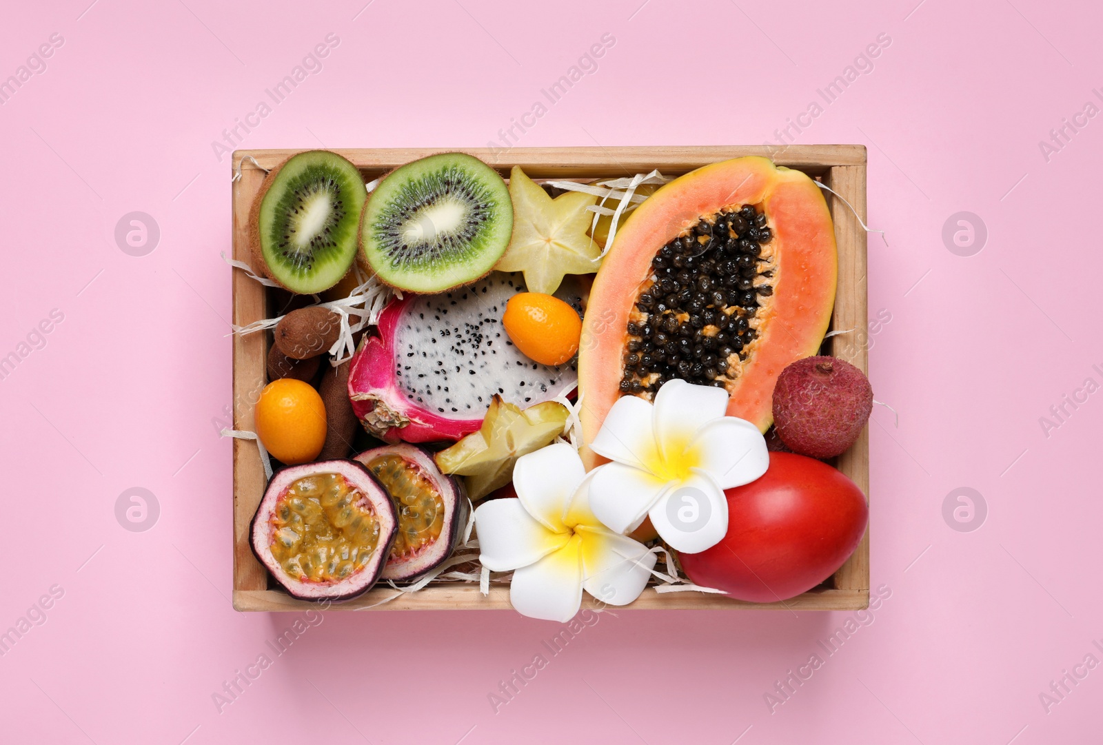Photo of Different tropical fruits in wooden box on pink background, top view