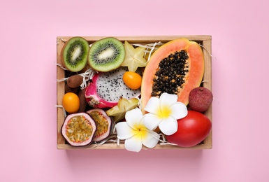 Different tropical fruits in wooden box on pink background, top view