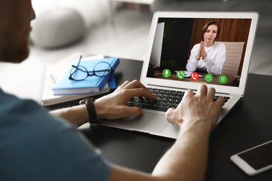 Image of Man using laptop at table for online consultation with psychologist via video chat, focus on screen