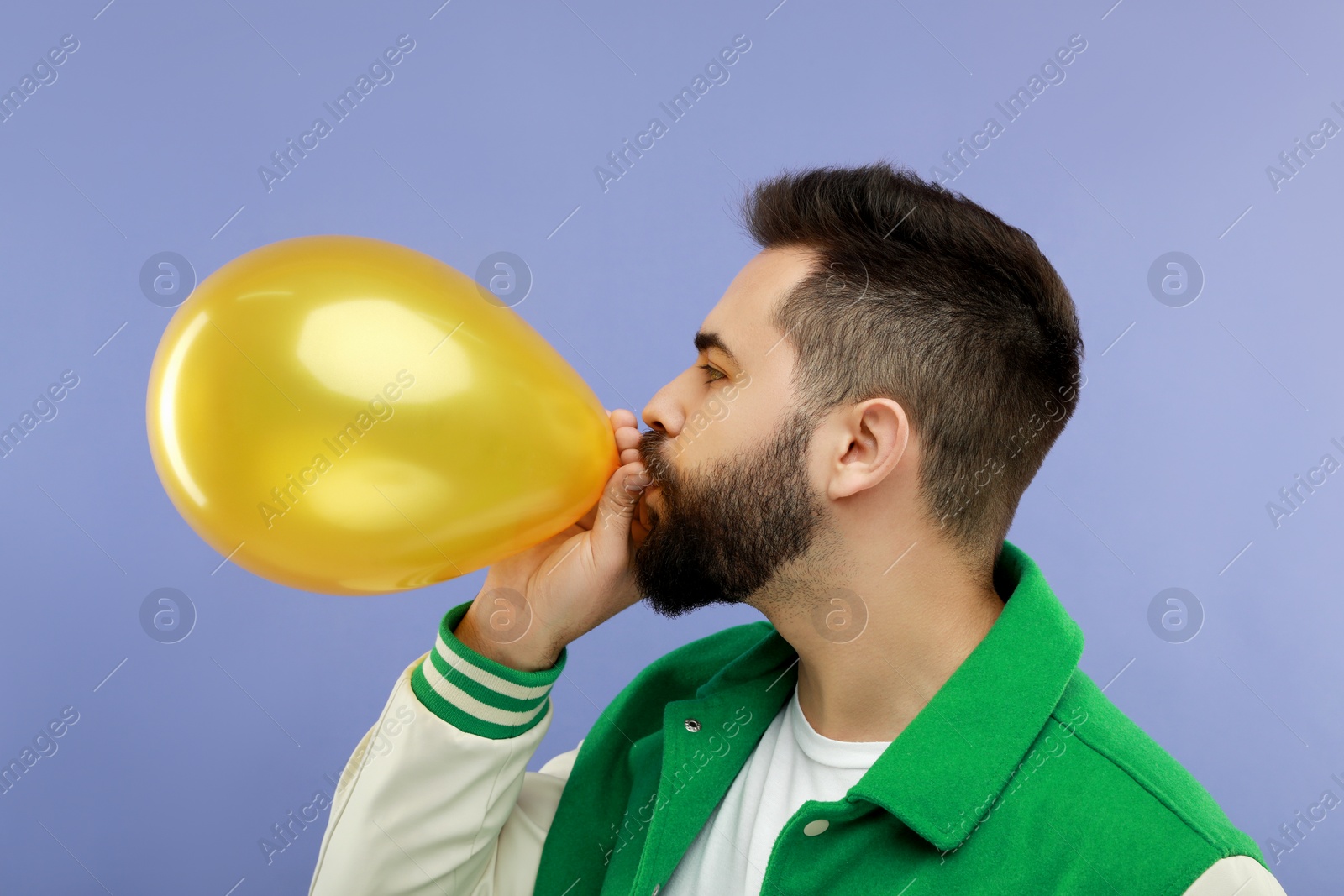 Photo of Man inflating bright balloon on violet background