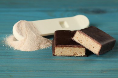 Photo of Pieces of tasty bar and spoon with protein powder on wooden table