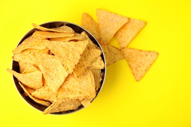 Bowl of tasty Mexican nachos chips on yellow background, top view