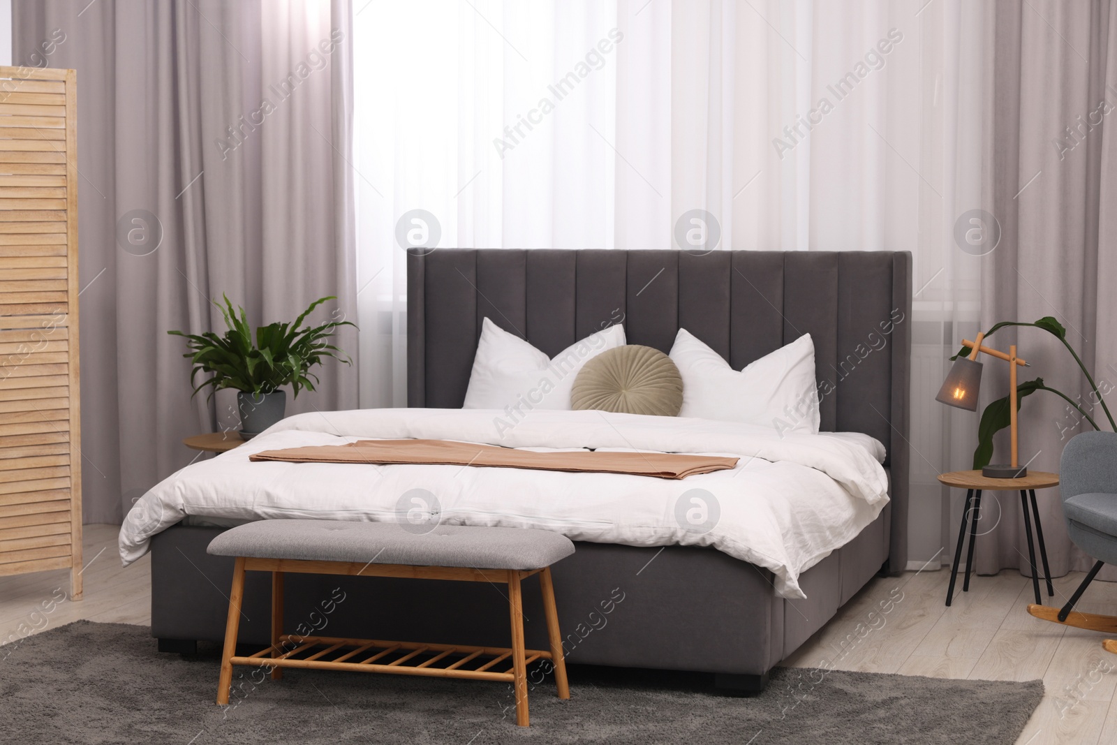 Photo of Stylish bedroom interior with large bed, ottoman, lamp and houseplants