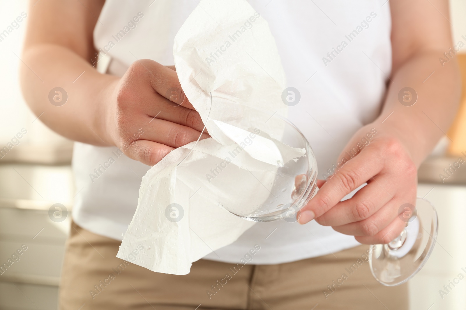 Photo of Woman wiping glass with paper towel in kitchen, closeup