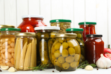 Glass jars with different pickled vegetables on white wooden background