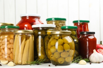 Photo of Glass jars with different pickled vegetables on white wooden background