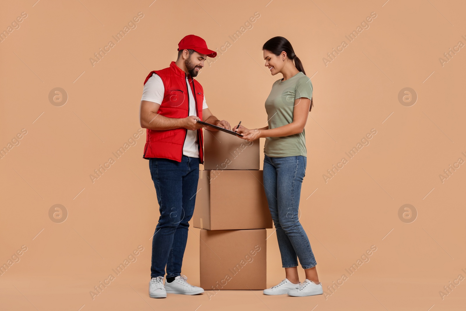 Photo of Smiling woman signing order receipt on light brown background. Courier delivery