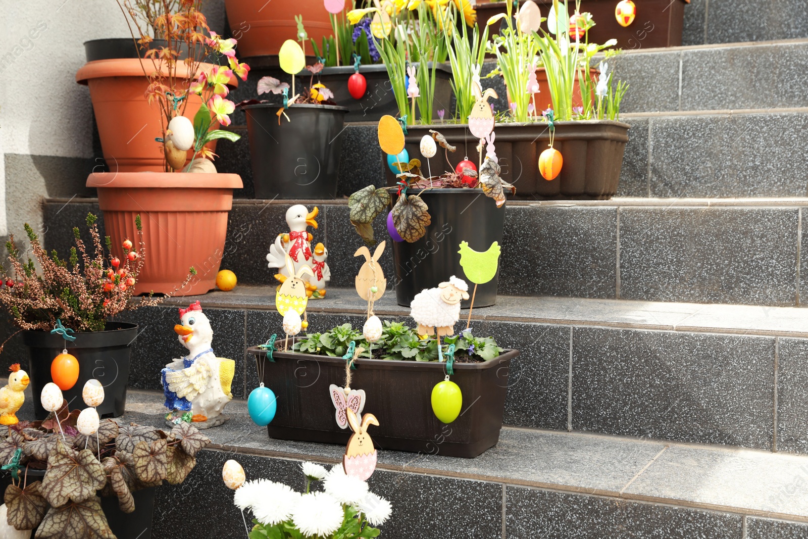 Photo of Beautiful plants with decorative eggs and different figures on stairs outdoors. Easter celebration