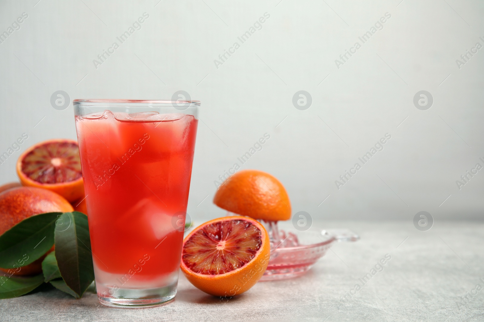 Photo of Tasty sicilian orange juice with ice cubes in glass, fruits and squeezer on light grey table, space for text