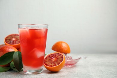 Photo of Tasty sicilian orange juice with ice cubes in glass, fruits and squeezer on light grey table, space for text