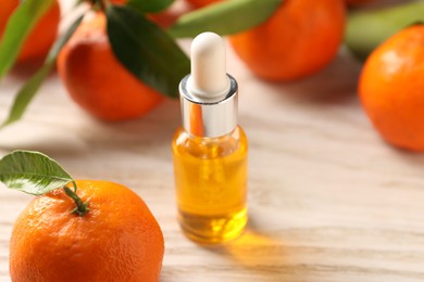 Bottle of tangerine essential oil and fresh fruits on white wooden table, closeup