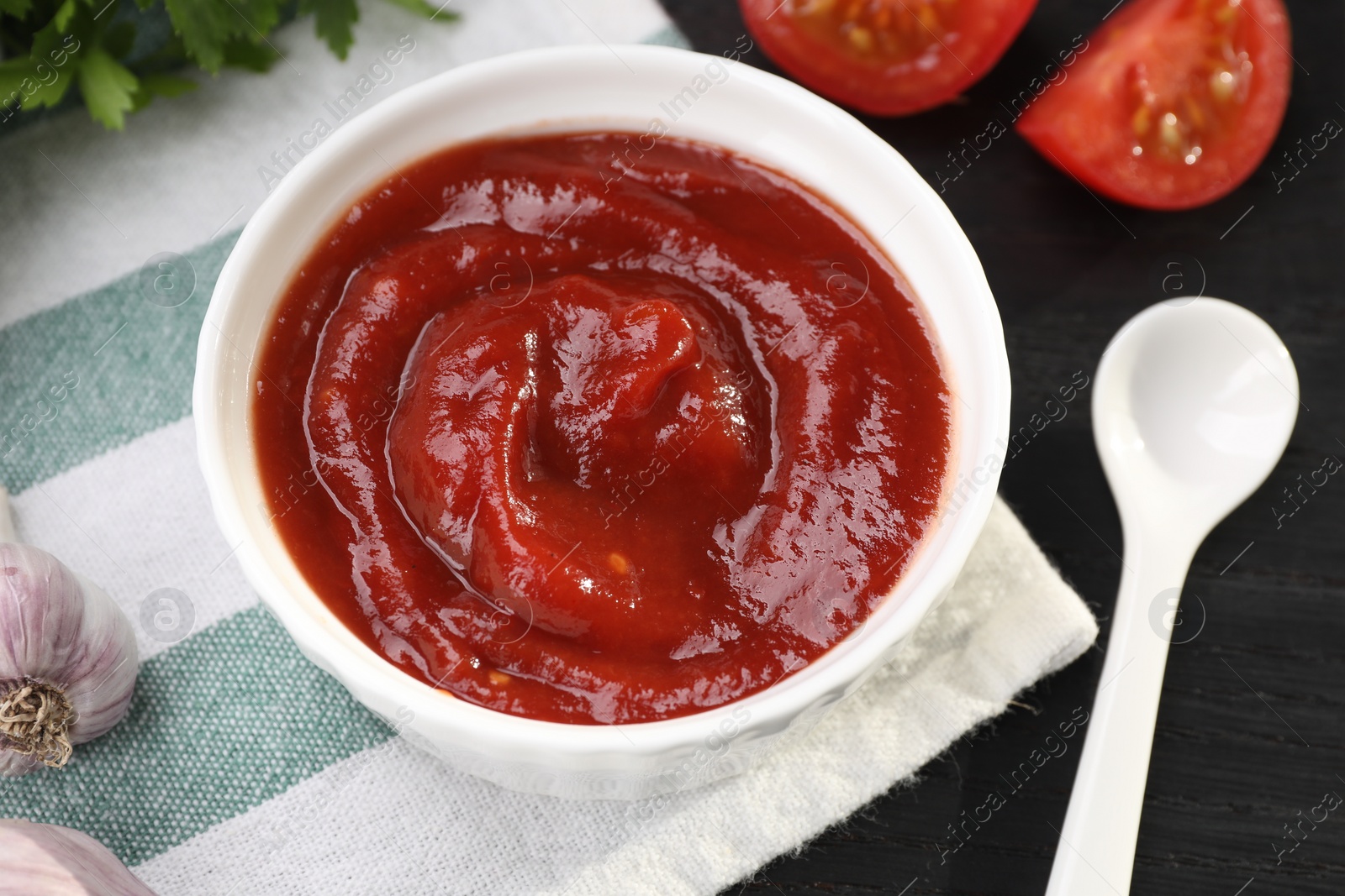 Photo of Organic ketchup in bowl on black table, closeup. Tomato sauce