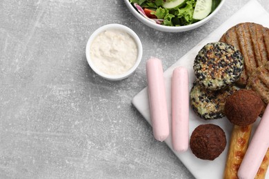 Photo of Different tasty vegan meat products, sauce and fresh vegetable salad on light grey table, flat lay. Space for text