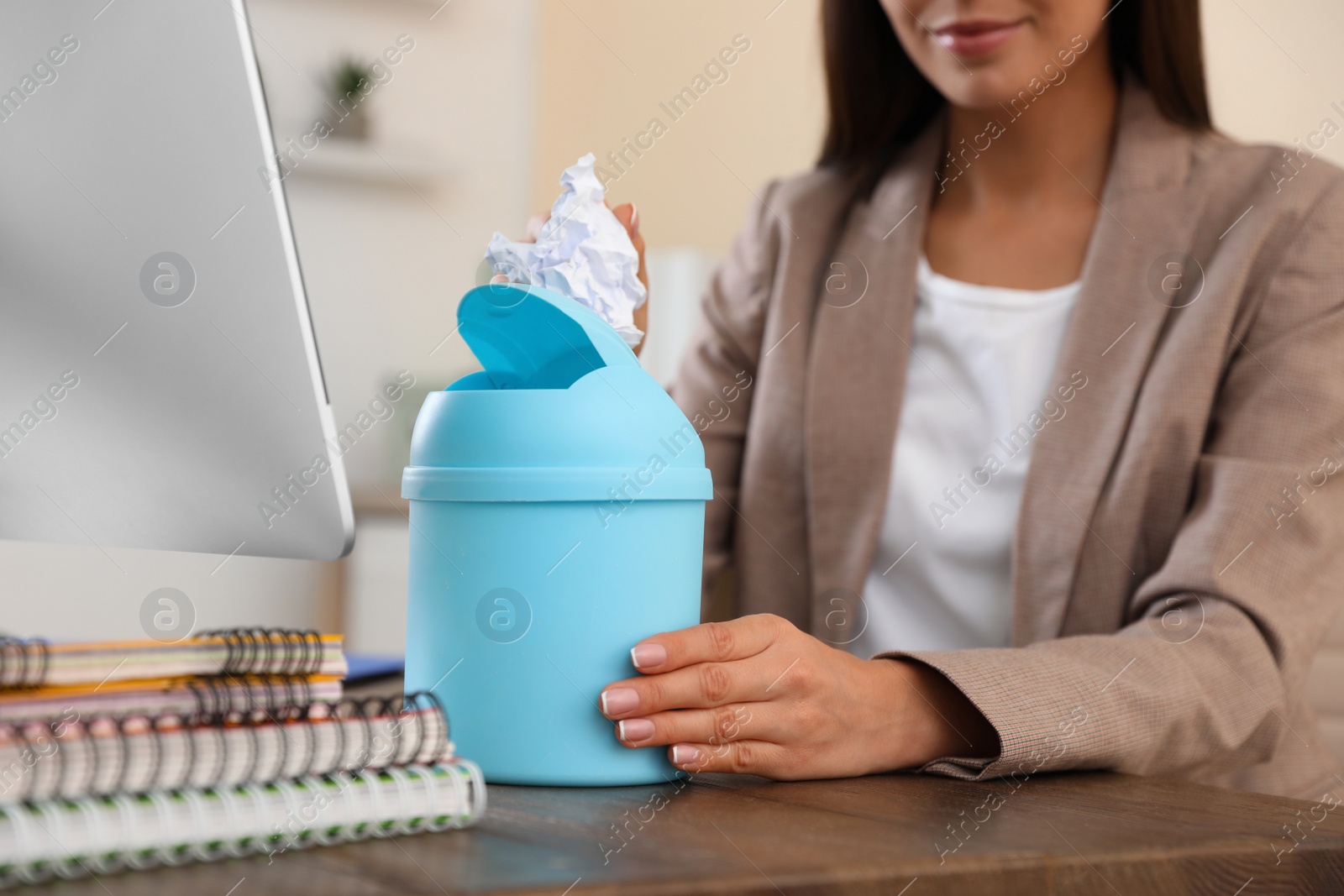 Photo of Young woman throwing paper into recycling bin at office, closeup