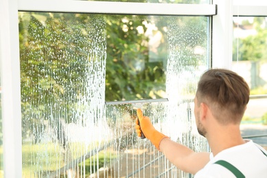 Photo of Male janitor cleaning window with squeegee indoors