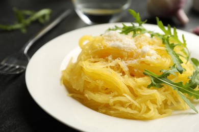 Photo of Tasty spaghetti squash with cheese and arugula 
 served on black table, closeup