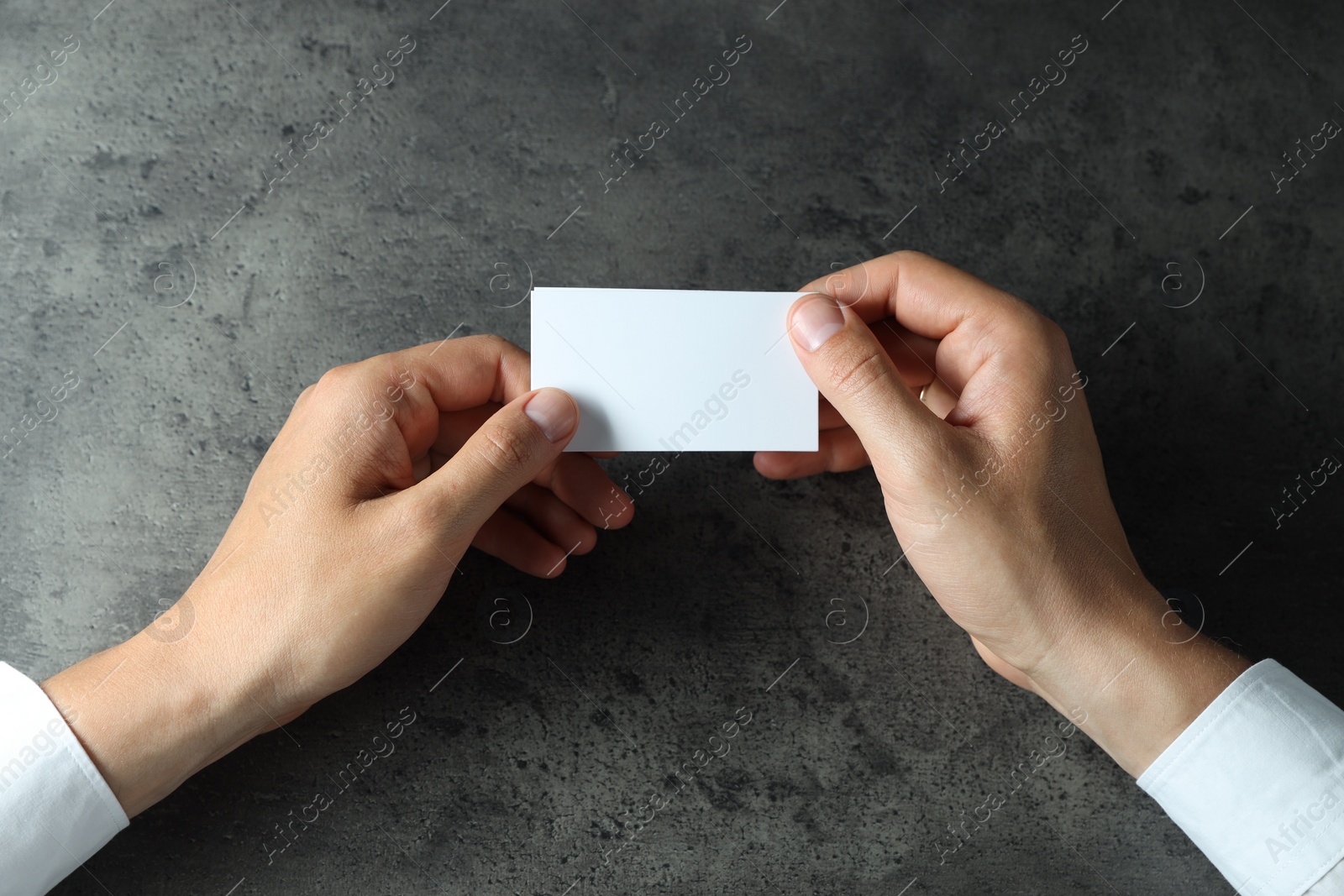 Photo of Man holding blank cards at black textured table, top view. Mockup for design