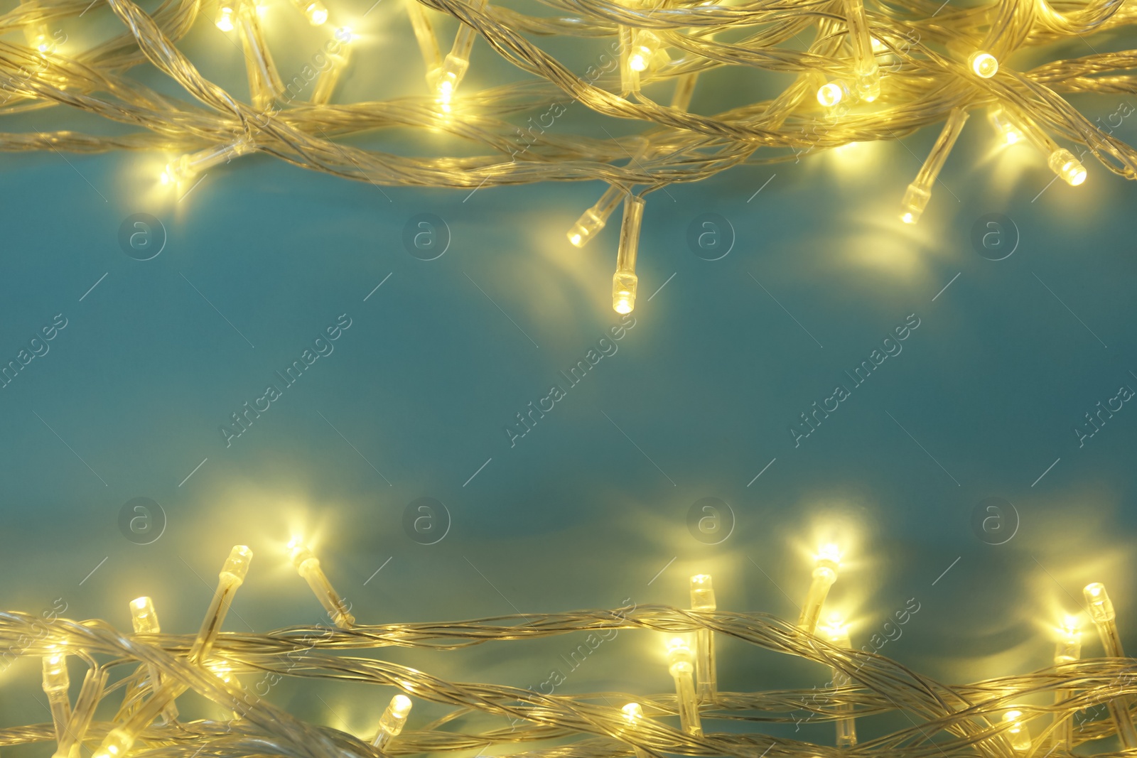 Photo of Glowing Christmas lights on blue background, top view. Space for text