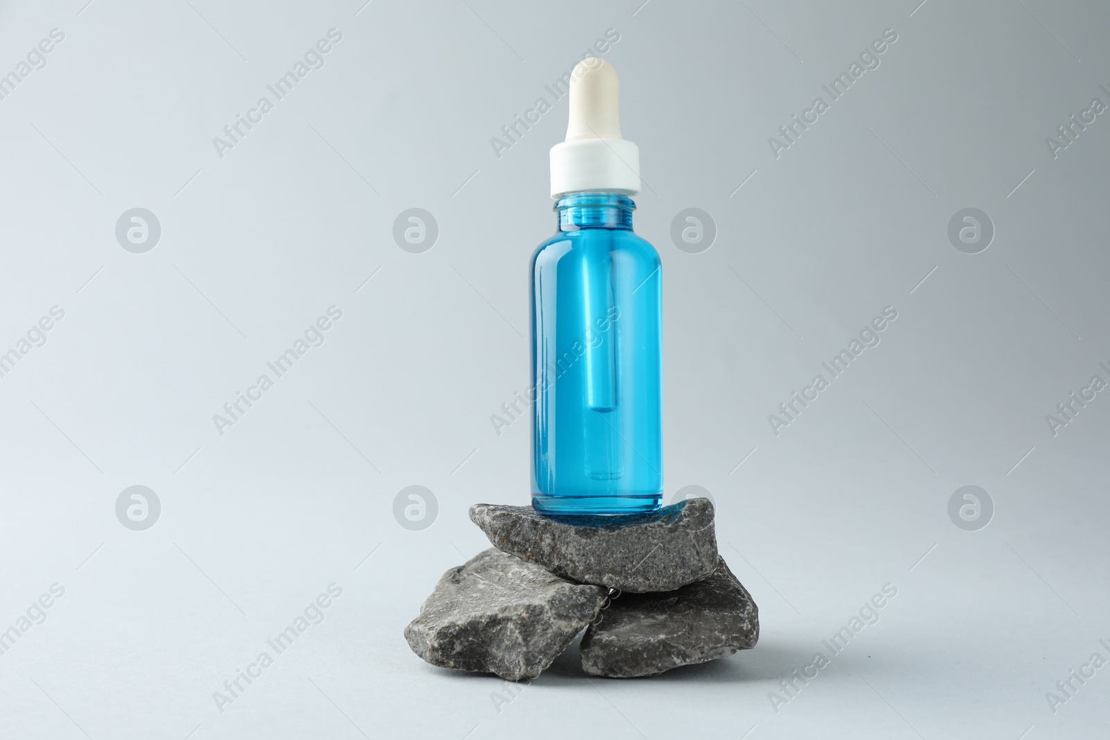 Photo of Bottle of cosmetic serum on stones against light grey background
