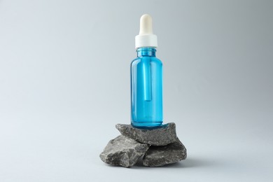 Bottle of cosmetic serum on stones against light grey background