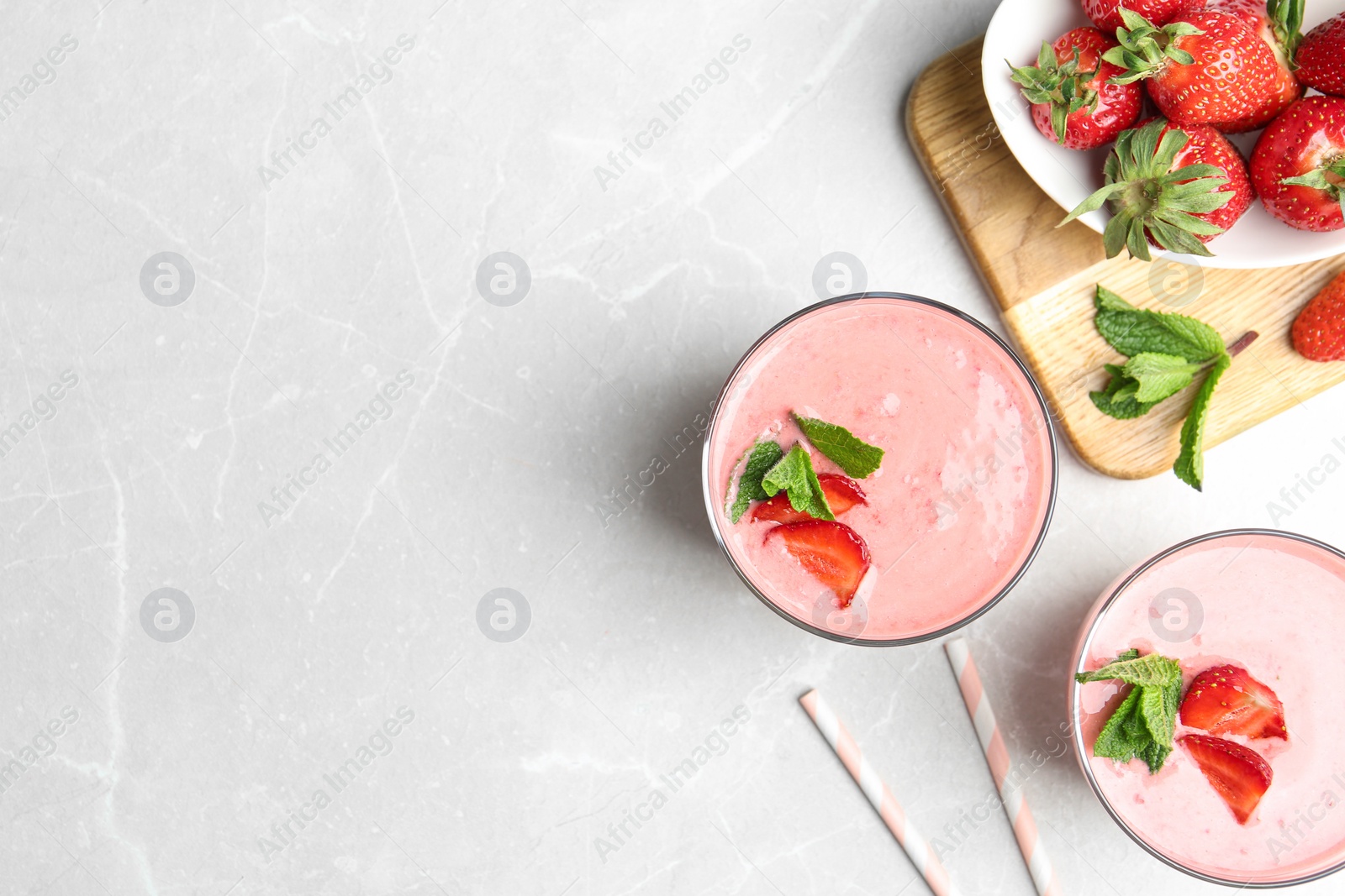 Photo of Tasty strawberry smoothies with mint in glasses on light grey marble table, flat lay. Space for text