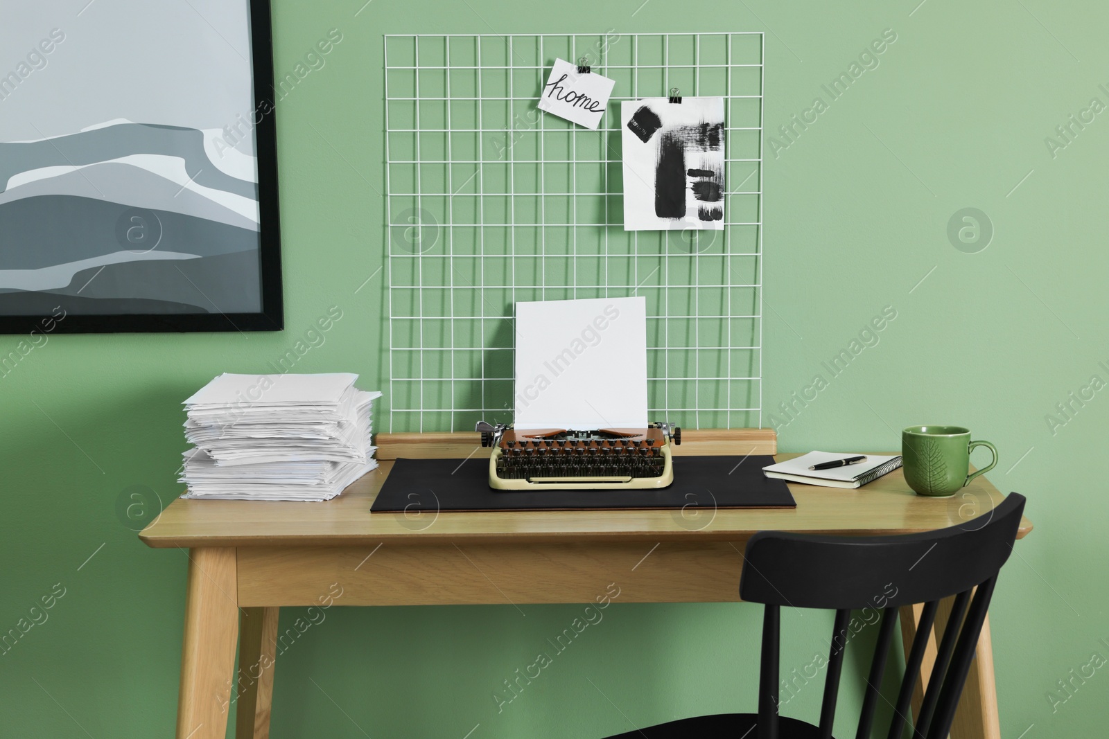 Photo of Typewriter, stack of papers and mood board on wooden table near pale green wall. Writer's workplace