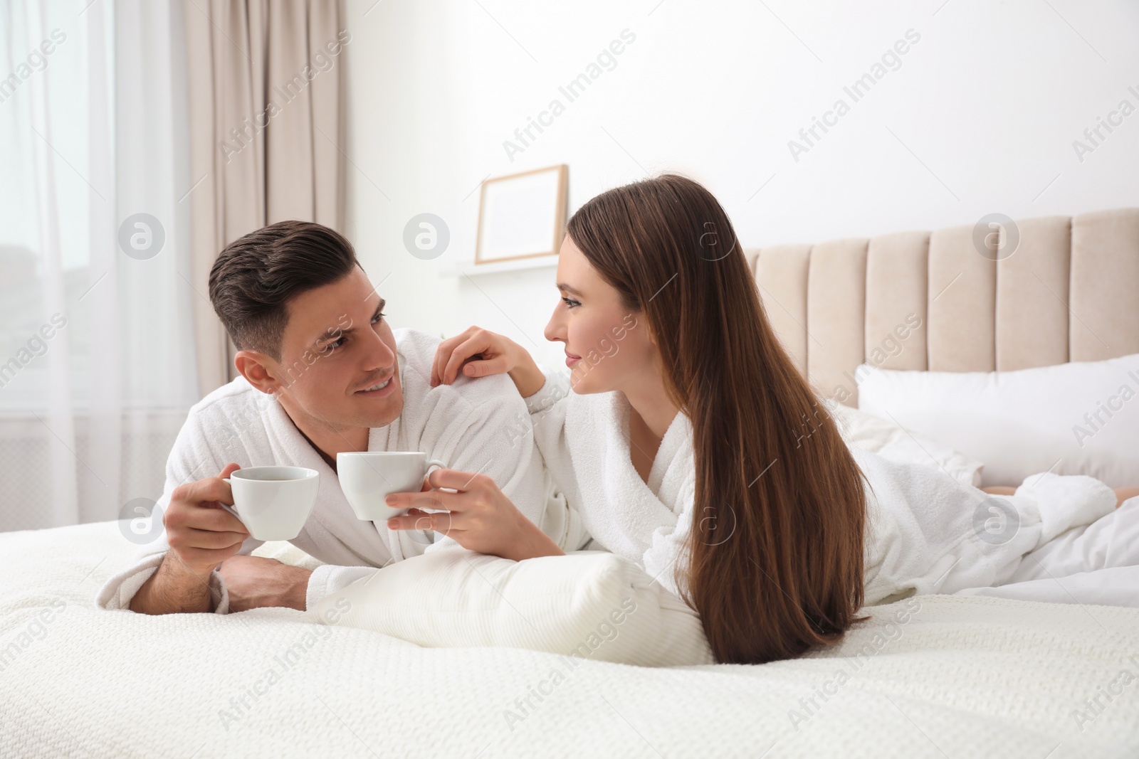 Photo of Happy couple in bathrobes with coffee on bed at home