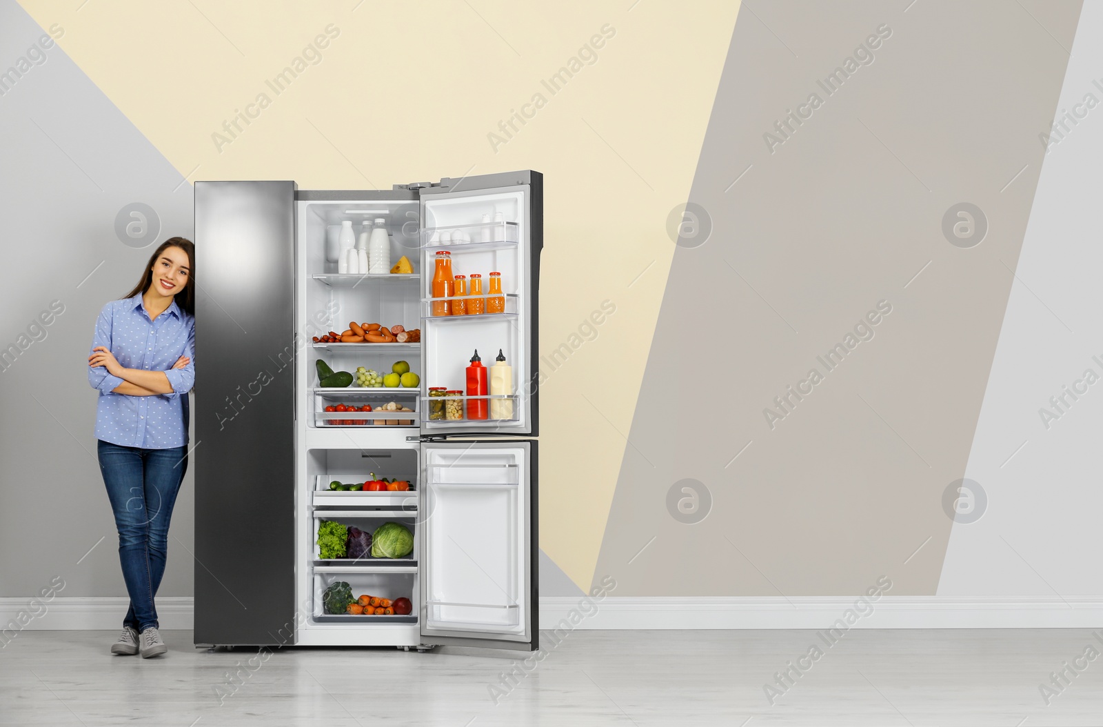 Photo of Happy young woman near open refrigerator indoors, space for text