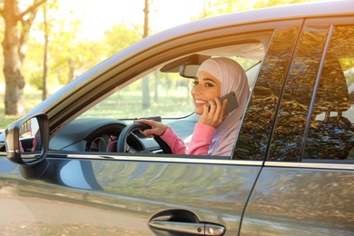 Muslim woman talking on phone in driver's seat of car