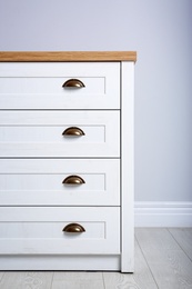 Photo of Stylish chest of drawers near white wall. Furniture for wardrobe room