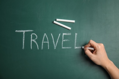 Photo of Woman writing word TRAVEL on chalkboard, top view. Tourist agency