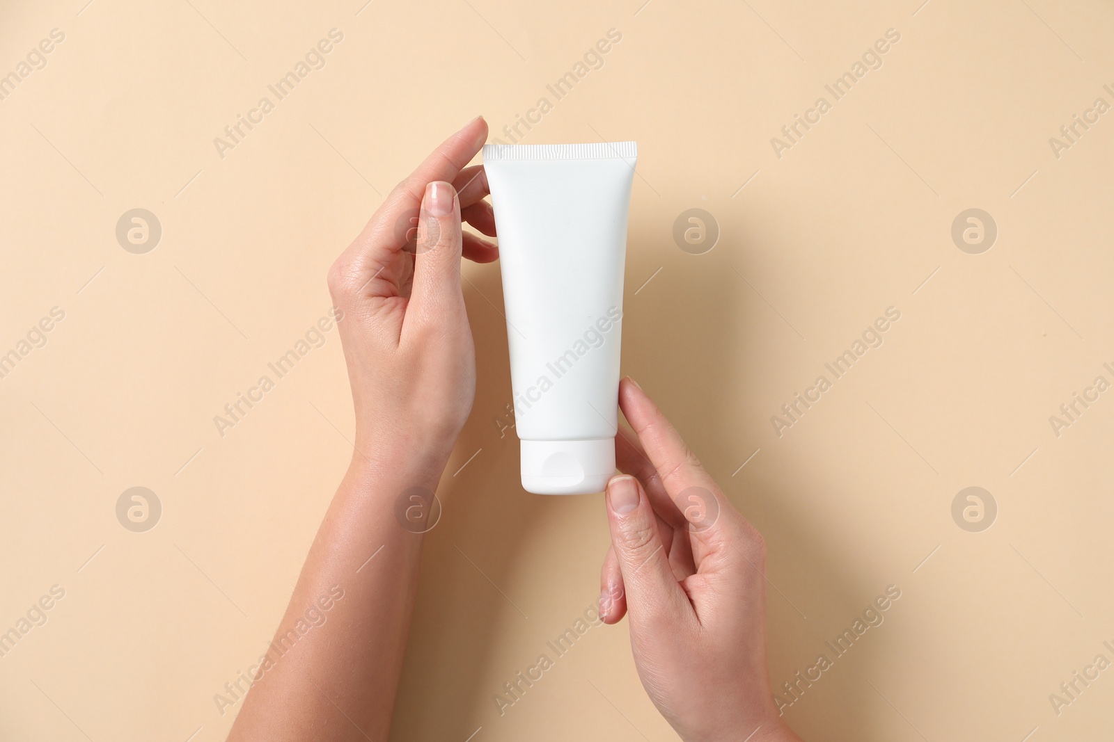 Photo of Woman with tube of hand cream on beige background, top view