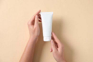 Photo of Woman with tube of hand cream on beige background, top view