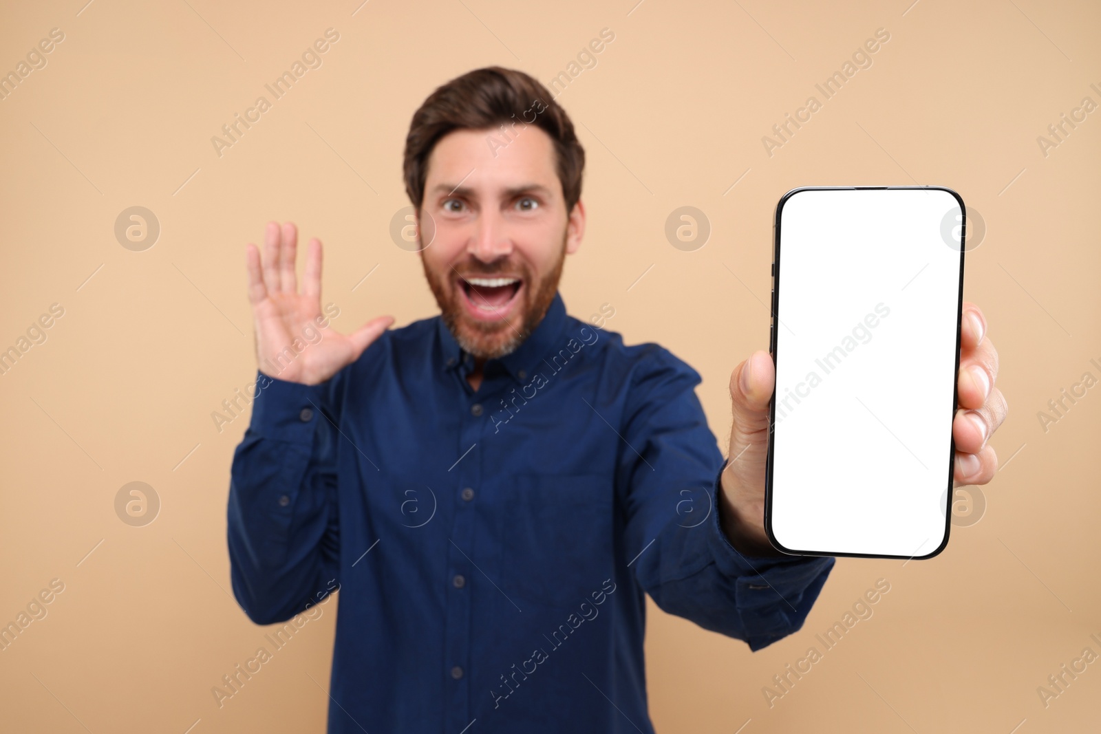 Photo of Surprised man showing smartphone in hand on light brown background, selective focus. Mockup for design