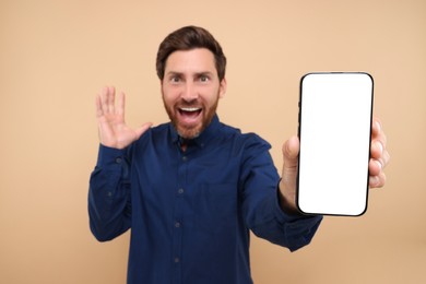 Photo of Surprised man showing smartphone in hand on light brown background, selective focus. Mockup for design