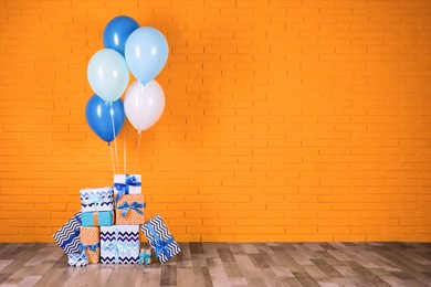 Many gift boxes and balloons near orange brick wall. Space for text