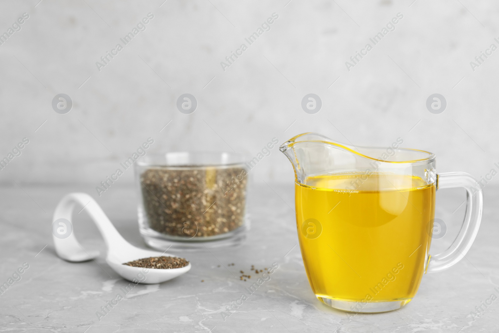 Photo of Composition with jug of chia seeds oil and grains on grey table. Space for text