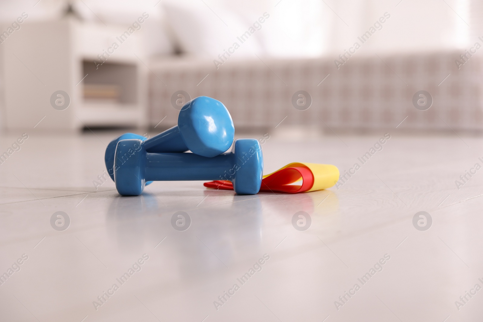 Photo of Dumbbells and different elastic bands on floor in room. Home fitness