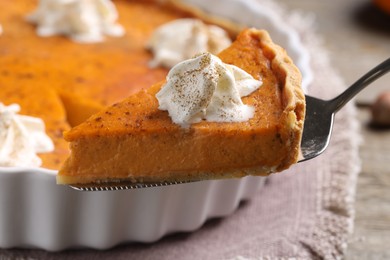 Piece of delicious pumpkin pie with whipped cream on server over table, closeup