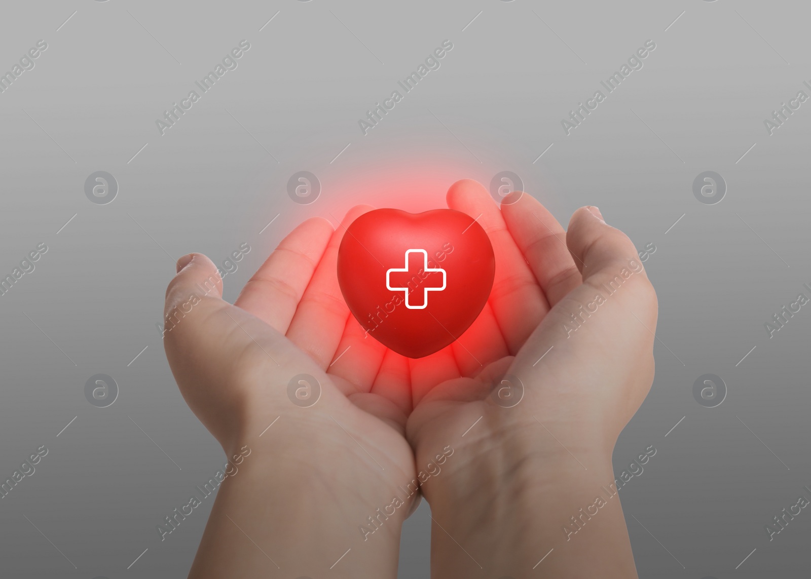 Image of Woman holding red heart in hands on light grey background, closeup. Blood donation concept