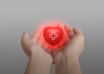 Image of Woman holding red heart in hands on light grey background, closeup. Blood donation concept