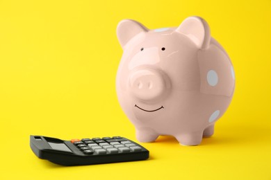 Photo of Calculator and pink piggy bank on yellow background
