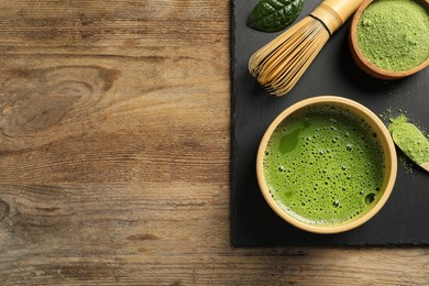Photo of Cup of fresh matcha tea, green powder and bamboo whisk on wooden table, top view. Space for text