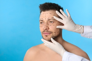 Photo of Doctor examining man's face before plastic surgery operation on blue background