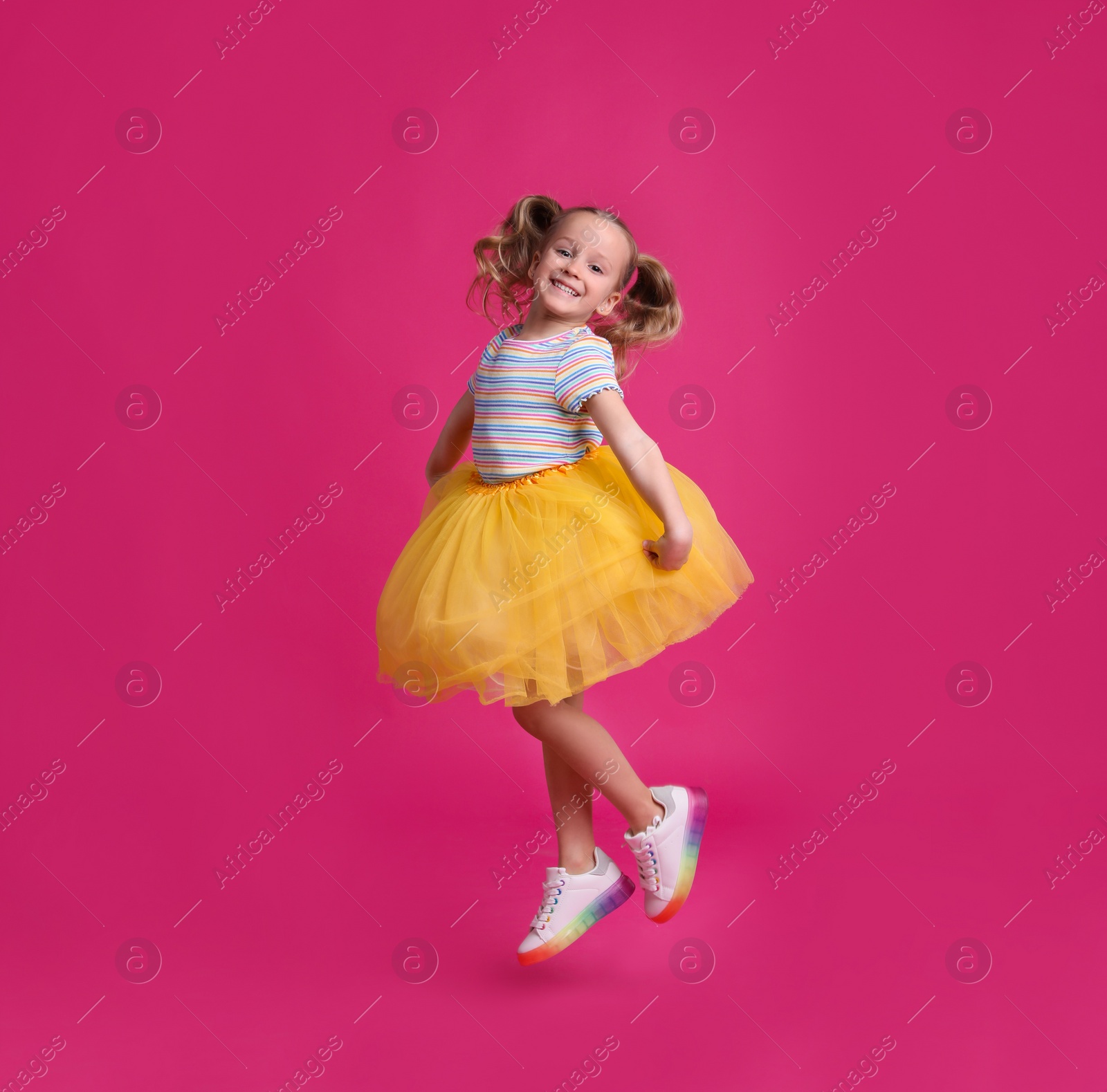 Photo of Cute little dancer in tutu skirt jumping on pink background