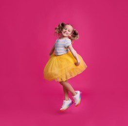 Photo of Cute little dancer in tutu skirt jumping on pink background