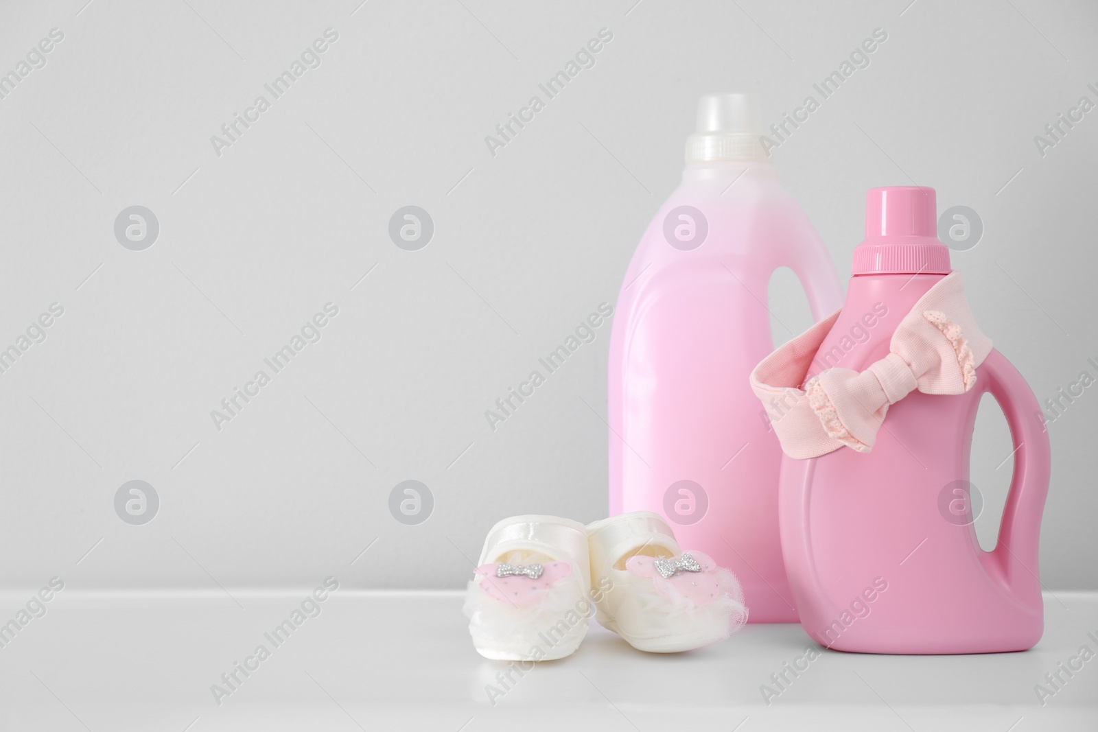 Photo of Bottles of detergent and children's clothes on white table. Space for text