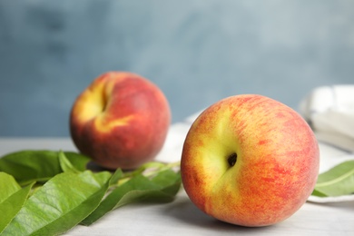 Tasty fresh peaches with leaves on white table against blue background